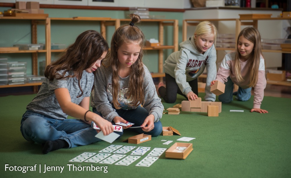 Bild på två barn som leker med nummerlappar och två till barn i bakgrunden som leker med klossar. Fotograf: Jenny Thörnberg.