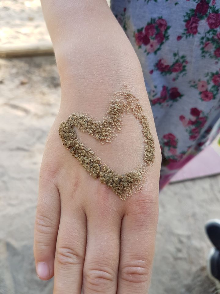 Närbild på handen till ett barn på en strand. Det finns sand på handen som är format som ett hjärta.