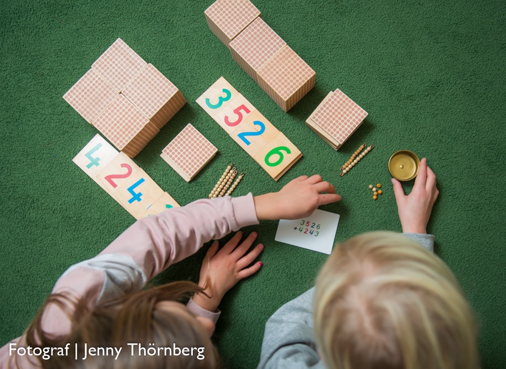 Bild på två barn som sitter på en grön matta och leker med ett matematikpussel som består av klossar och siffror.